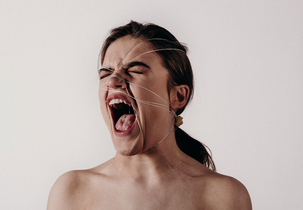 Symbolbild Gewalt: schreiende Frau mit geschlossenen Augen, ihr Kopf ist mit einer Schnur verspannt, Credit: Noah Buscher, Unsplash