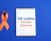 blaues Rechteck mit Multiple Sklerose Awareness-Schleife, darüber Notizblock mit Text: S2k-Leitlinie Multiple Sklerose. Credit: Canva