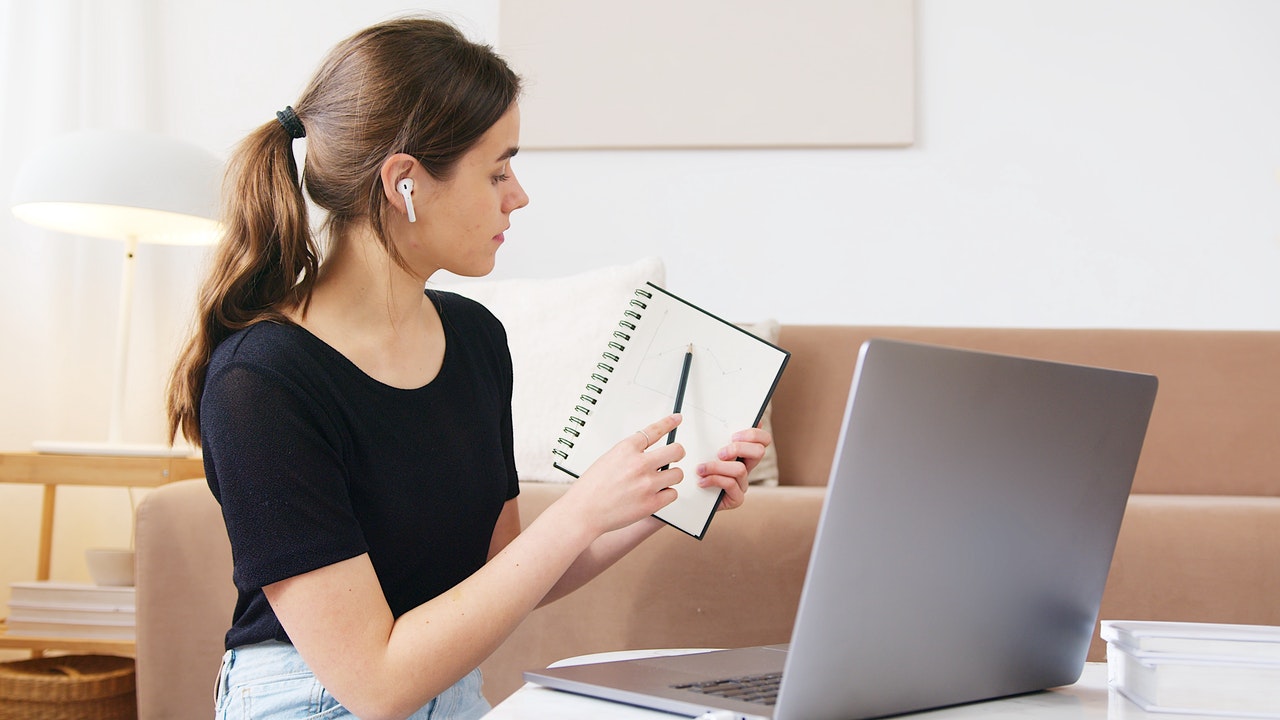 Frau sitzt vor Laptop und zeigt etwas auf ihrem Notizblock, Foto: Artem Podrez, Pexels